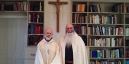 Br. John and Abbot smiling in front of crucifix and bookcase