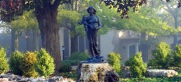 stature of Blessed Mother offering infant Jesus placed in wooded garden in front of a house