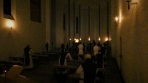 monks in darkened church, lit by candles