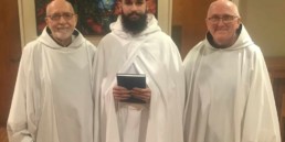 Br. Matthew enters novitiate, smiling holding book between abbot and Novice Director