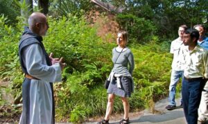 A monk speaks to visitors in a garden